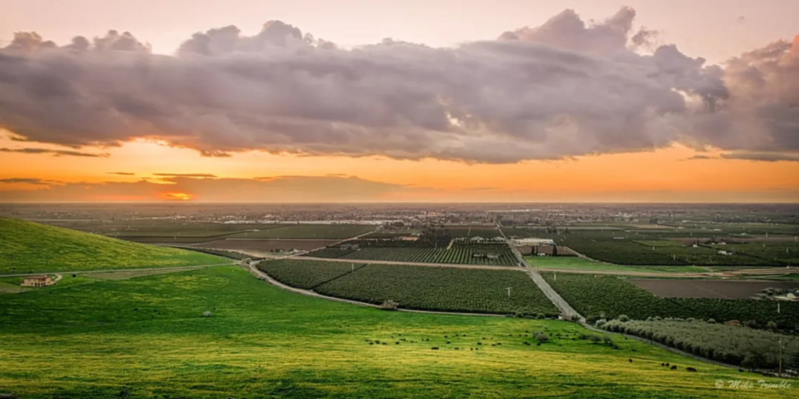 Sunset over green hills and agricultural landscape with cloudy sky