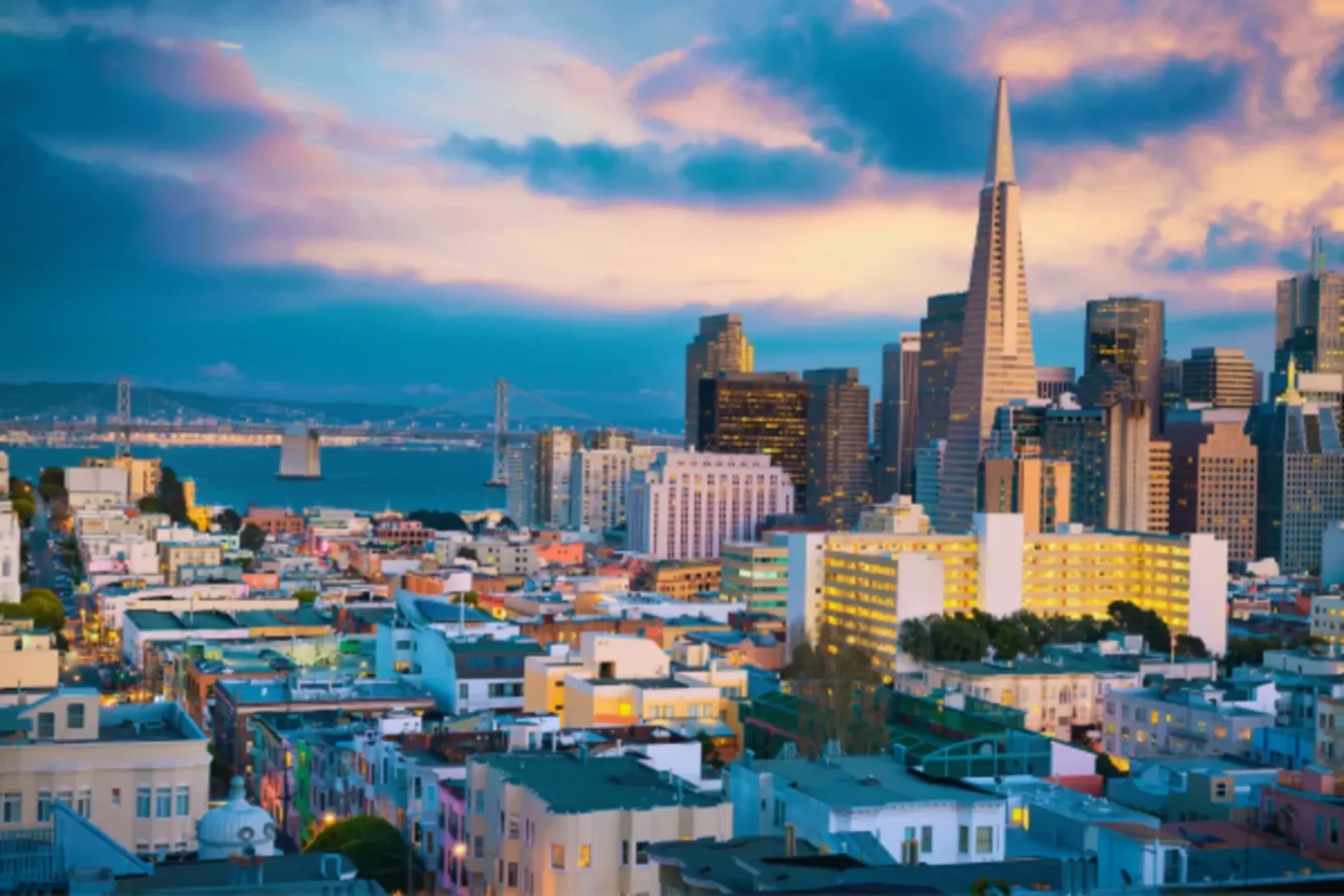 San Francisco skyline at dusk with Transamerica Pyramid, Bay Bridge, and colorful sunset clouds over the city.