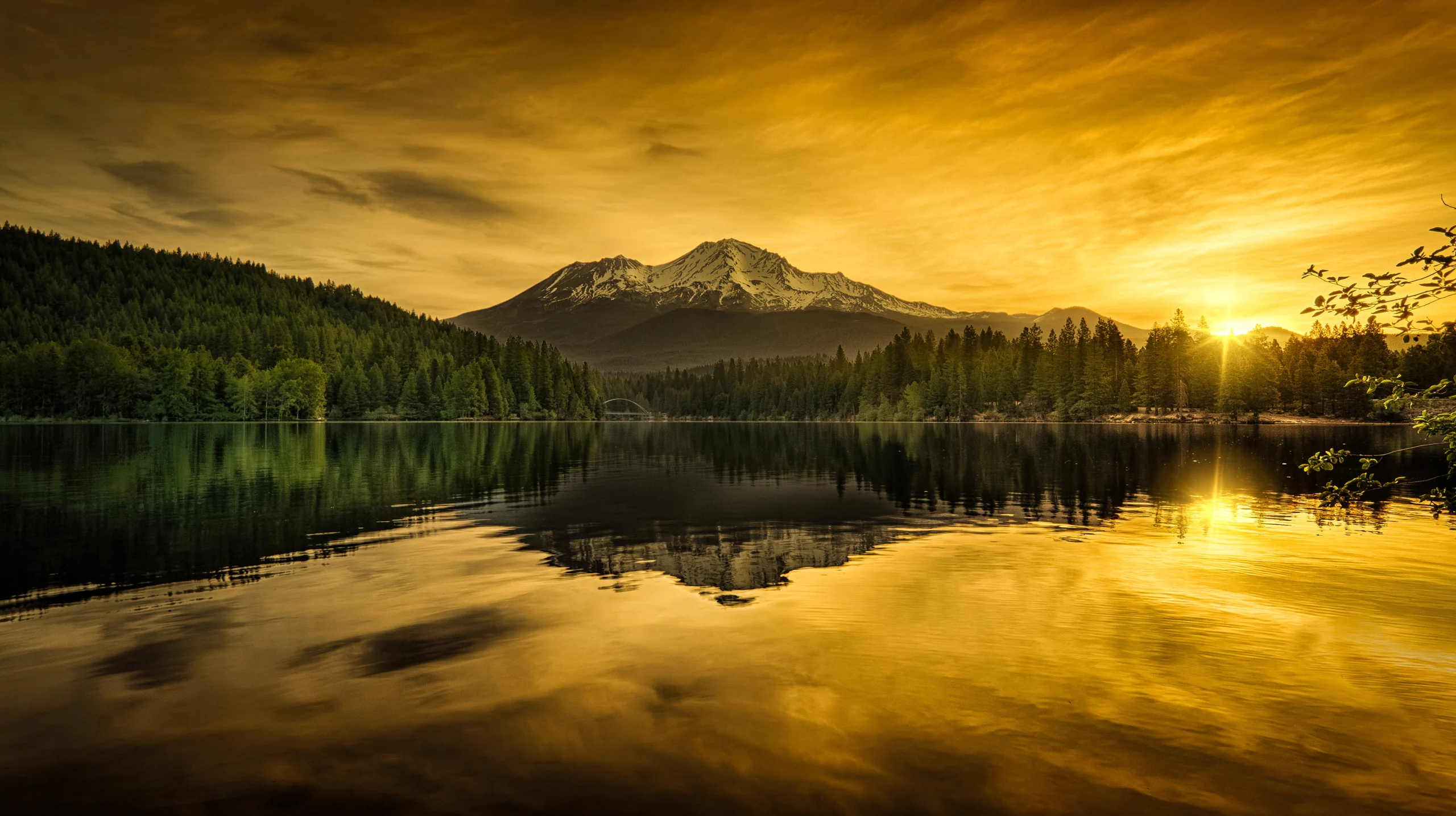 Golden sunset over mountain lake with forest reflection and dramatic sky in Northern California wilderness.