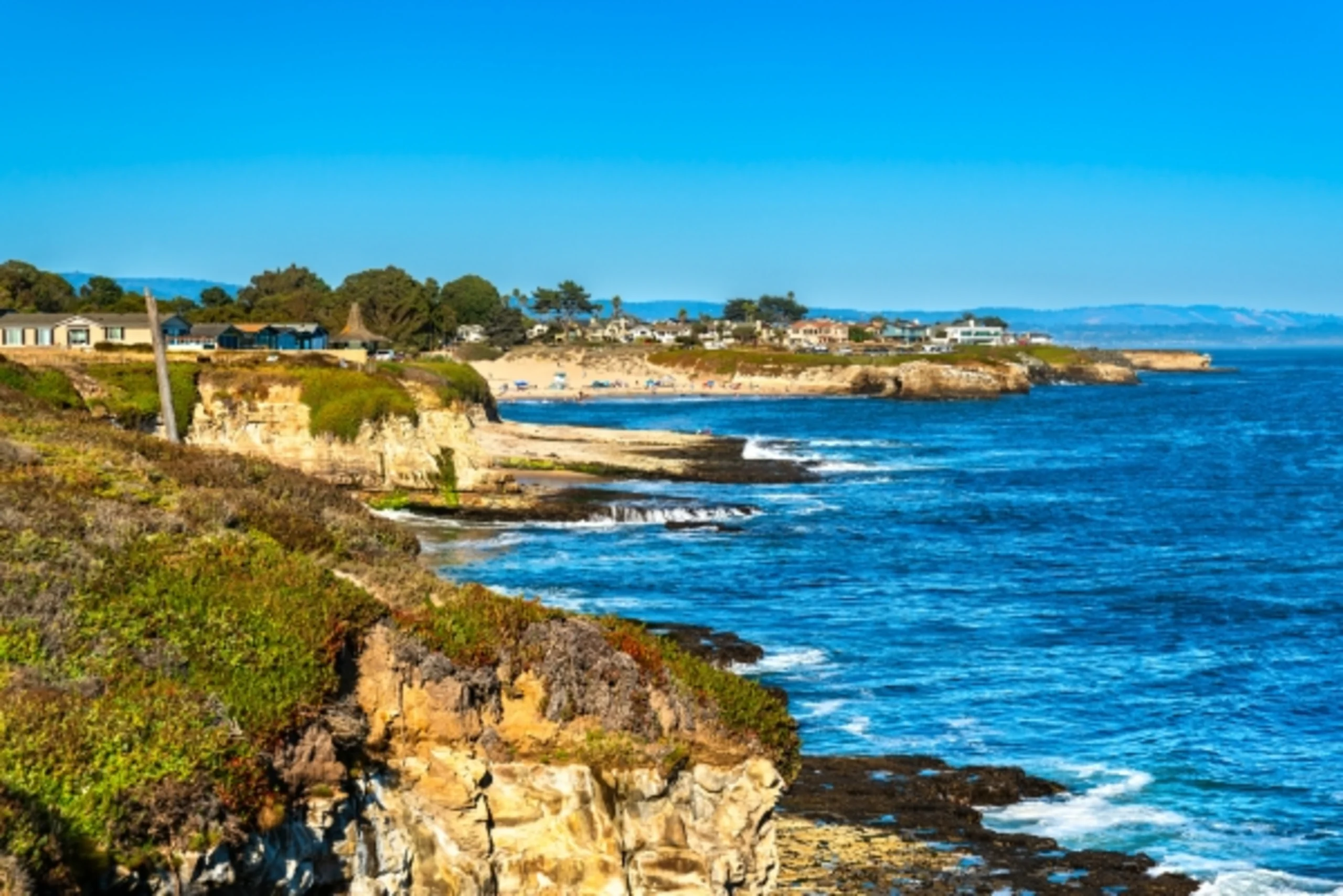 Scenic coastal cliffs with homes overlooking the blue Pacific Ocean on a sunny day in Central California.