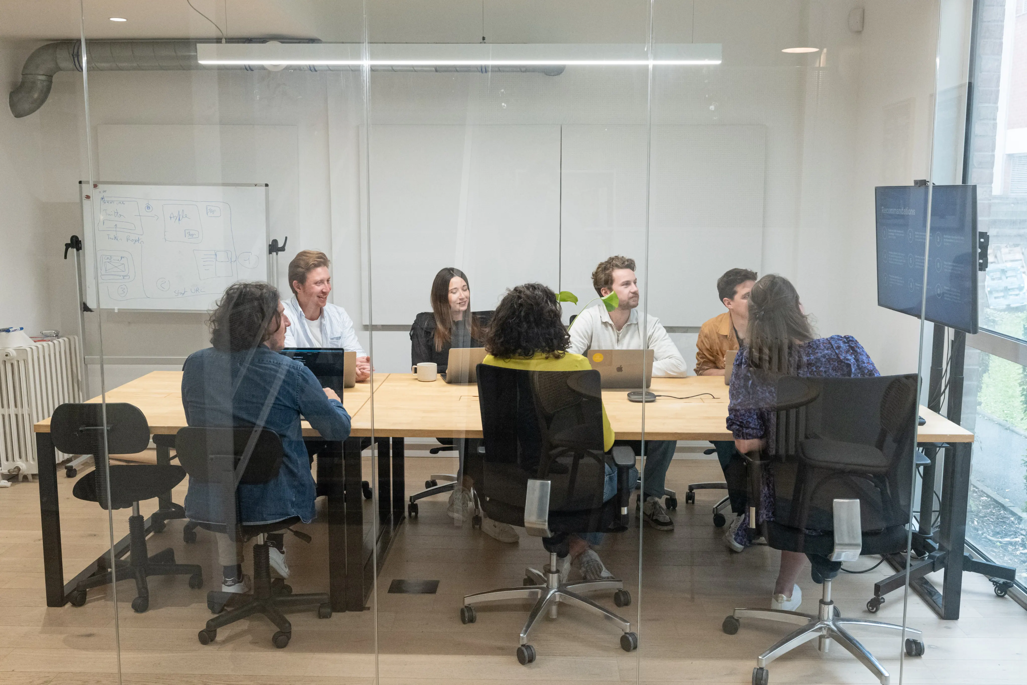 Équipe diversifiée en réunion dans une salle de conférence moderne avec un tableau blanc et un écran affichant des recommandations.