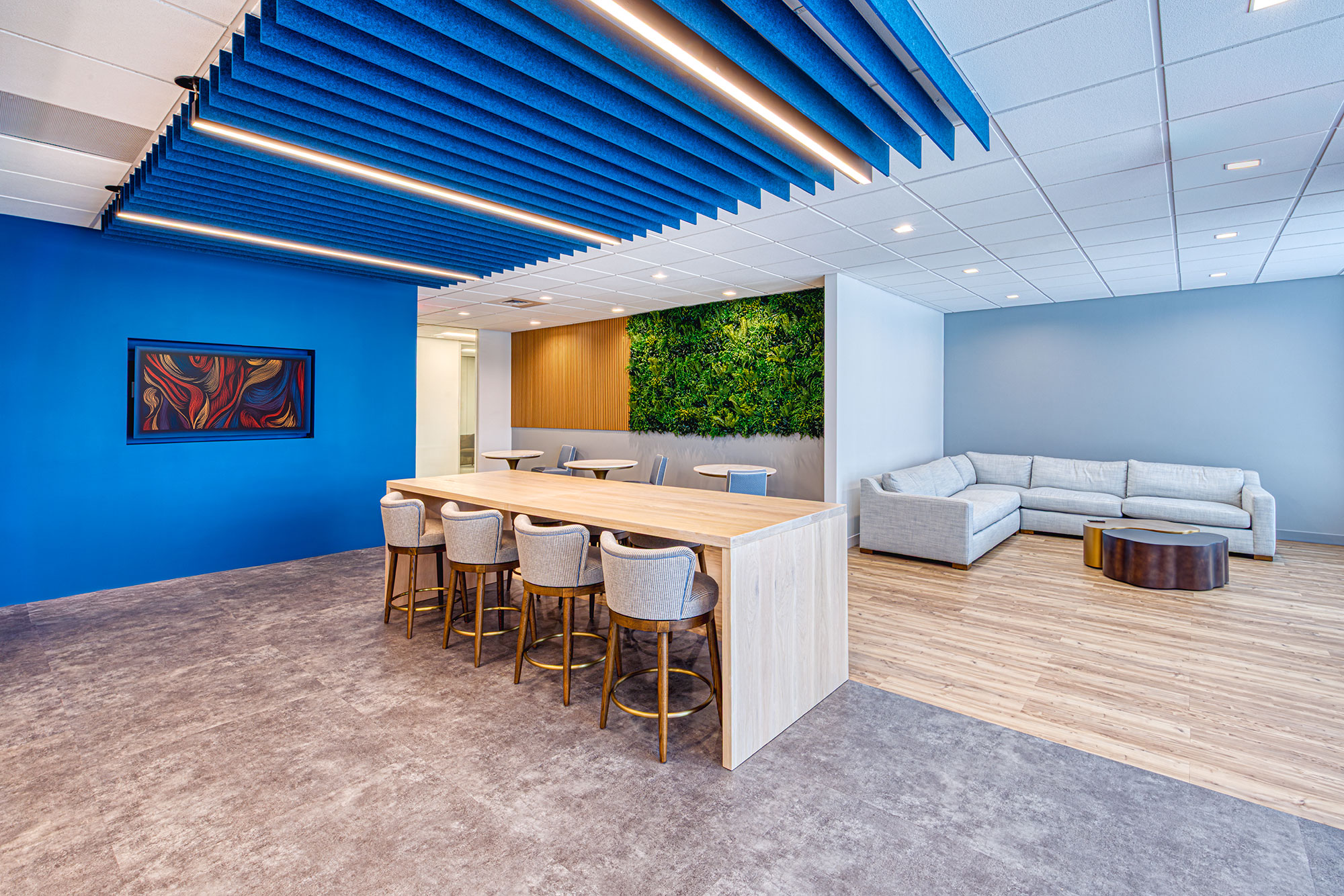 Collaboration zone by Ossa Studio with long island table, lounge seating, blue acoustic baffles and living wall; modern office design.