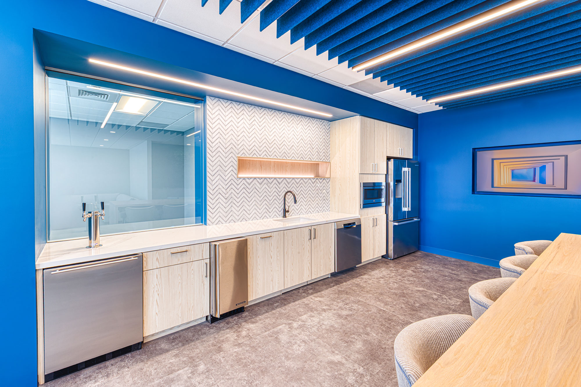 Kitchen detail by Ossa Studio showing beverage taps, chevron tile, light wood cabinetry and stainless appliances; contemporary office kitchen design.