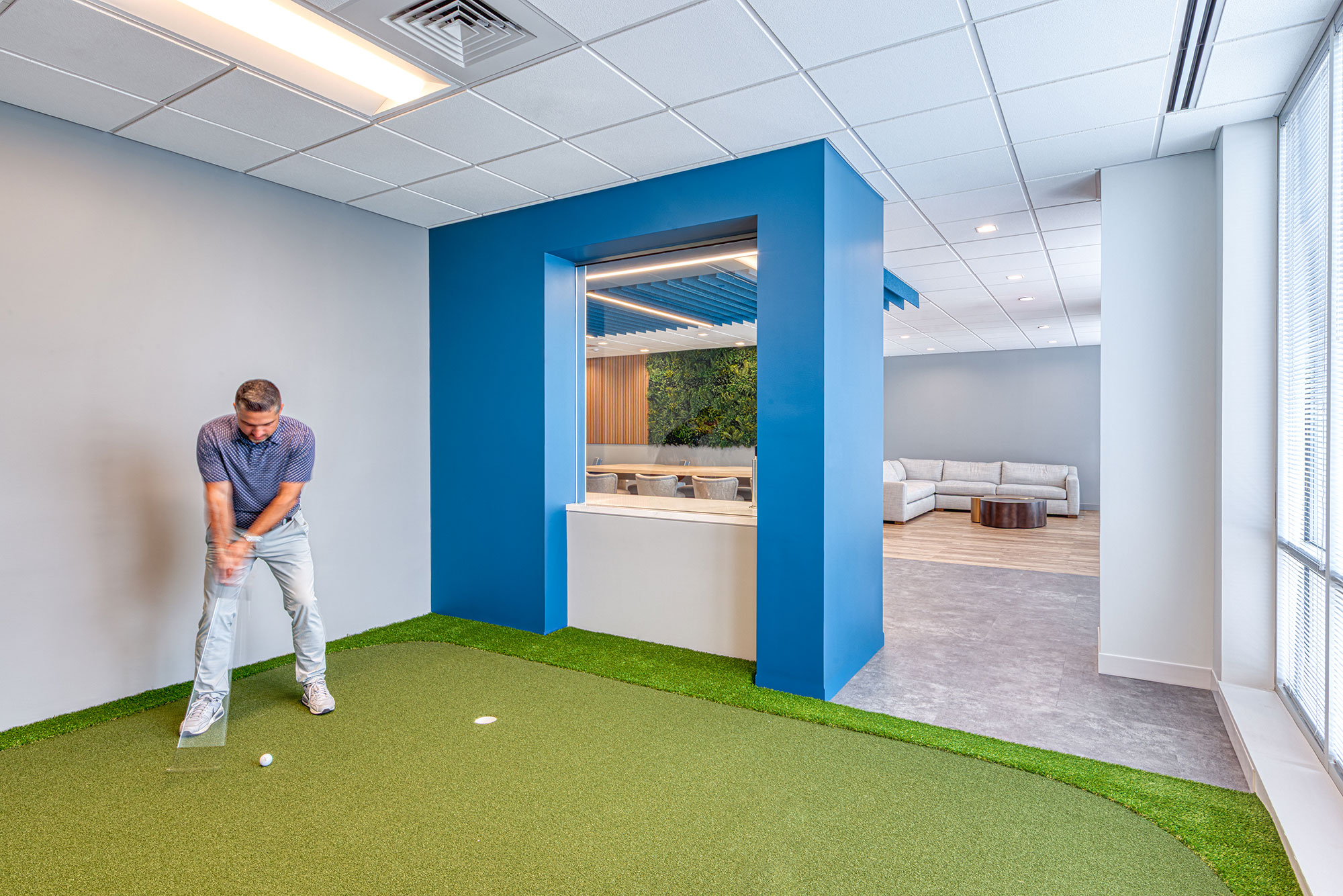 Indoor putting green amenity by Ossa Studio, framed by a blue portal and adjacent lounge; workplace wellness and employee experience.