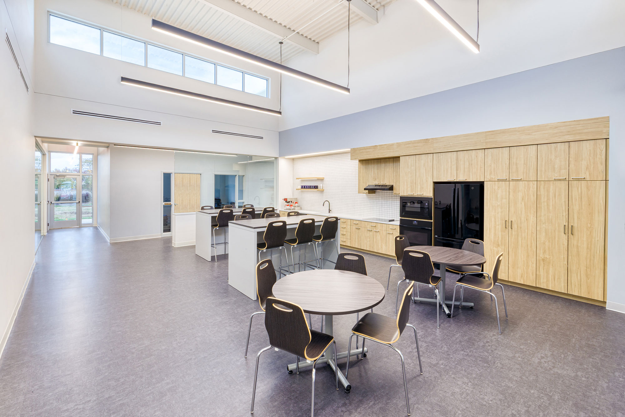 Open breakroom and cafeteria at Crowder Construction Expansion by Ossa Studio, with wood cabinetry, communal tables, high ceilings, and abundant natural light.