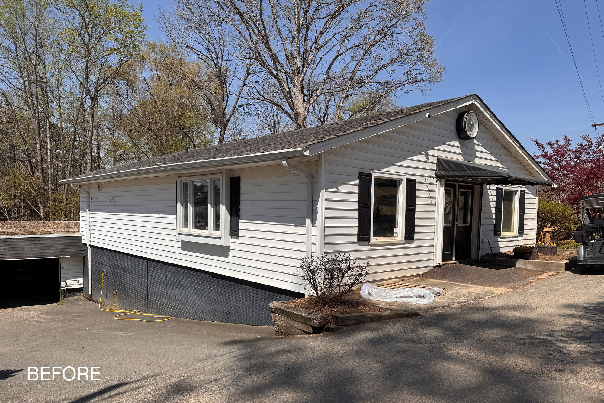 Side view of the Pine Lake pro shop and lower cart barn before renovation, with a painted brick base and vinyl siding.