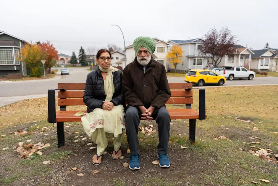 Elderly couple sitting on a bench in a suburban neighborhood during autumn, capturing a serene moment.