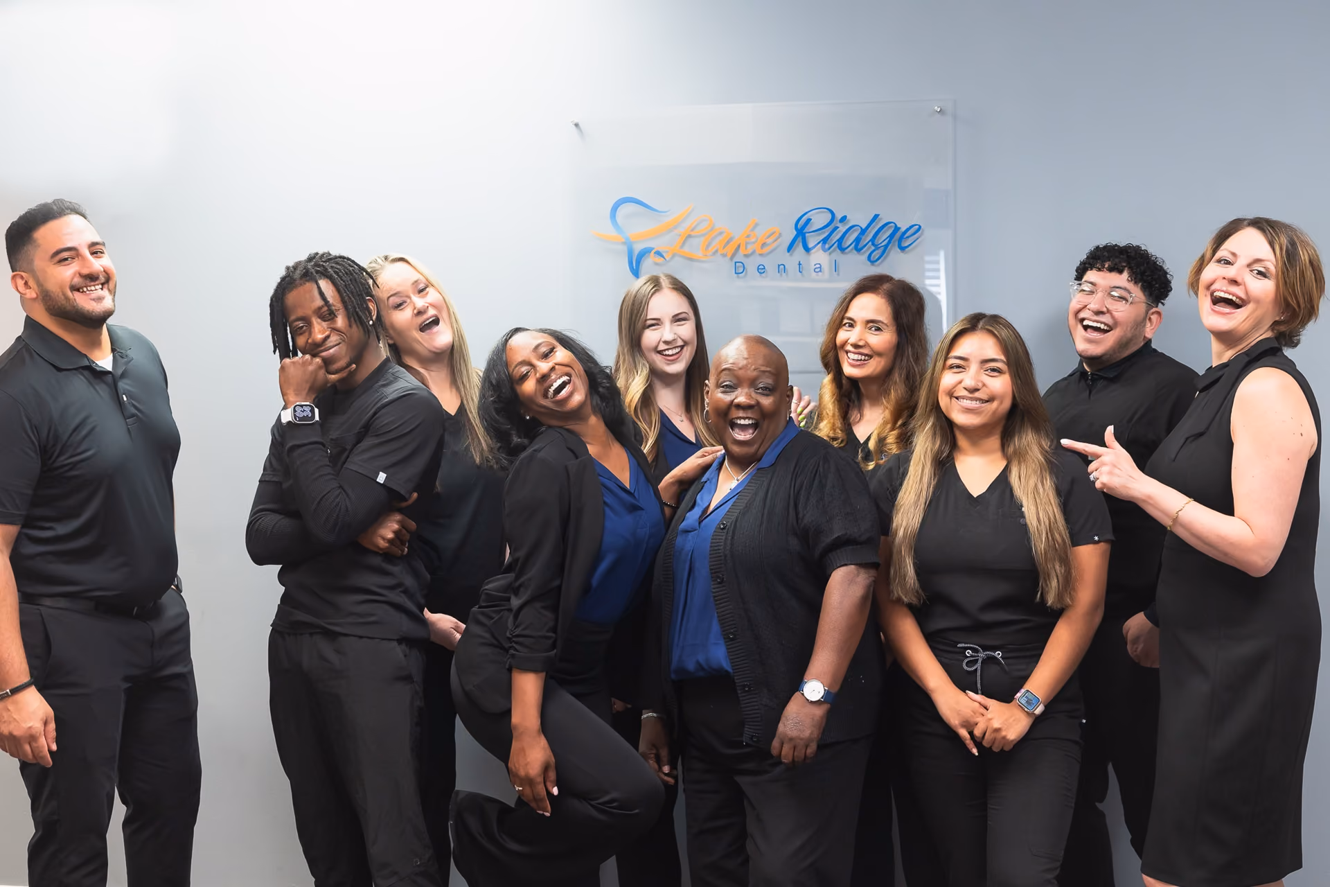Smiling diverse dental team of nine standing in front of Lake Ridge Dental sign.