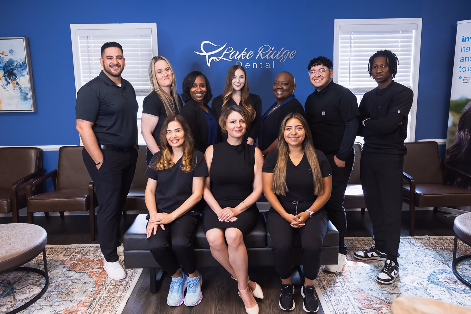 Group portrait of ten diverse dental staff members posing in the reception area of Lake Ridge Dental with blue walls and branded signage.