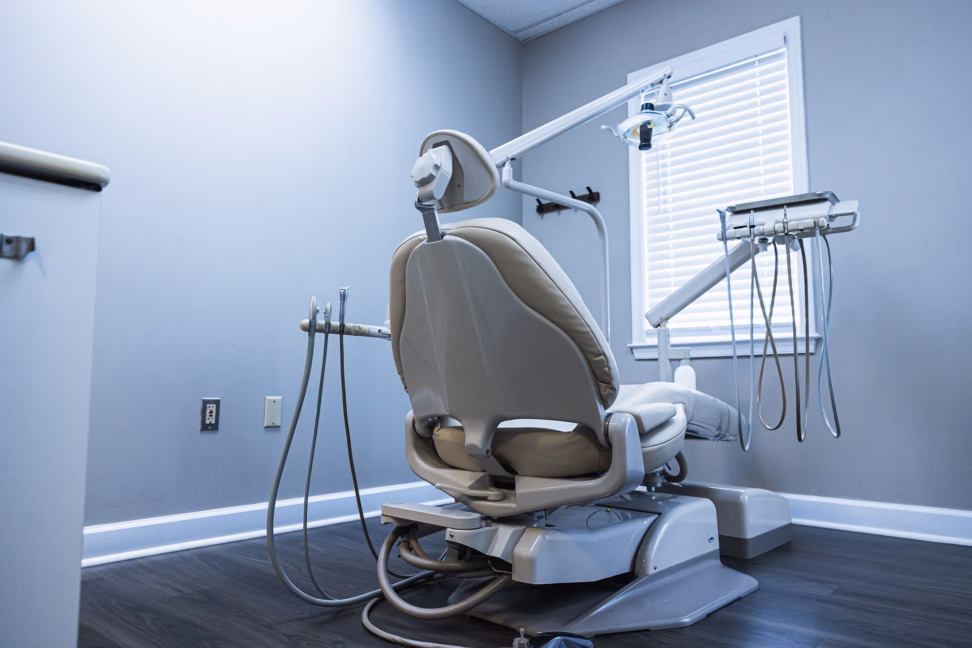 Empty beige dental chair with attached dental instruments in a clean, modern dental office room.
