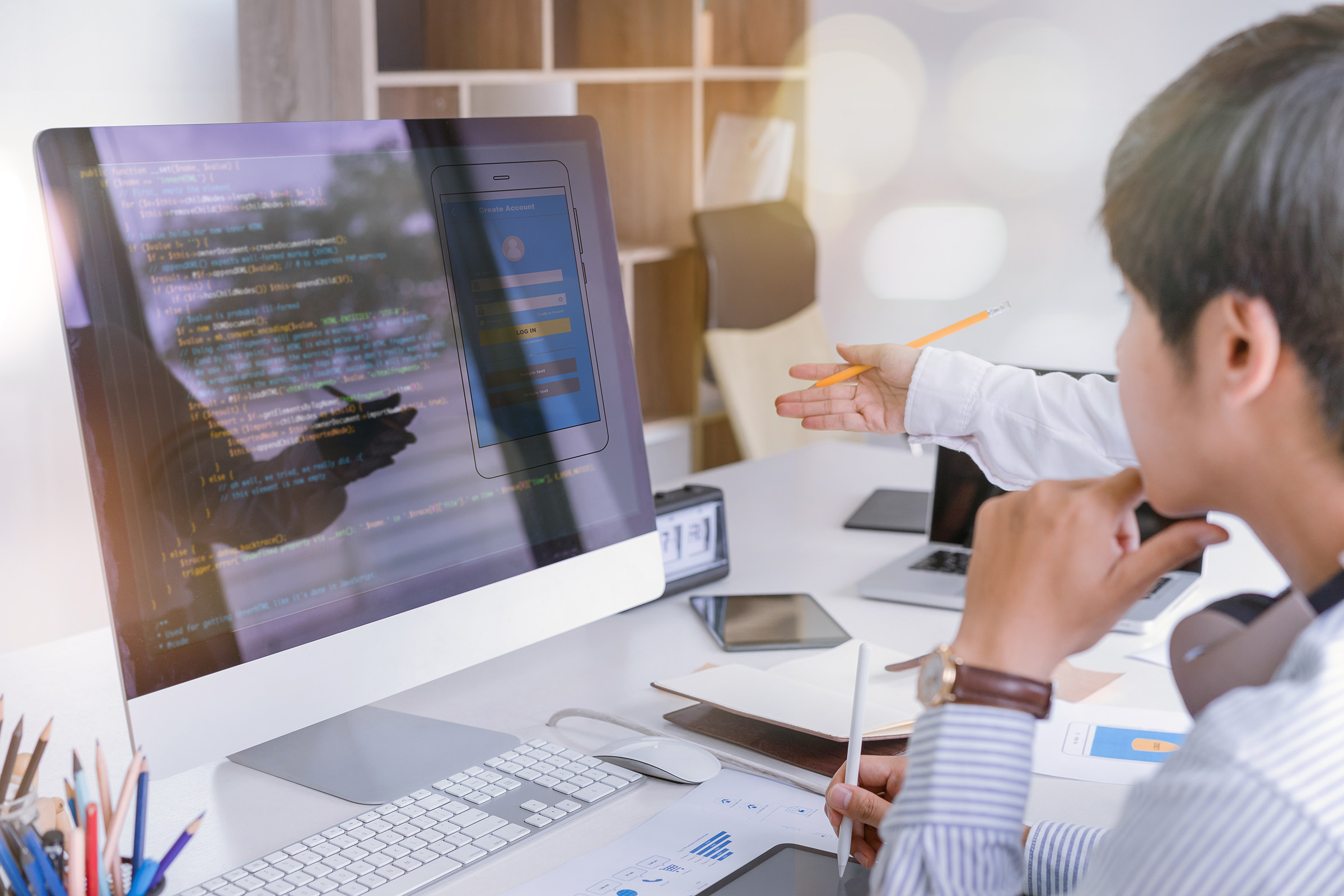 Front-end developers collaborating on UI design and coding at a desktop computer, with code and a mobile app mockup visible on the screen.