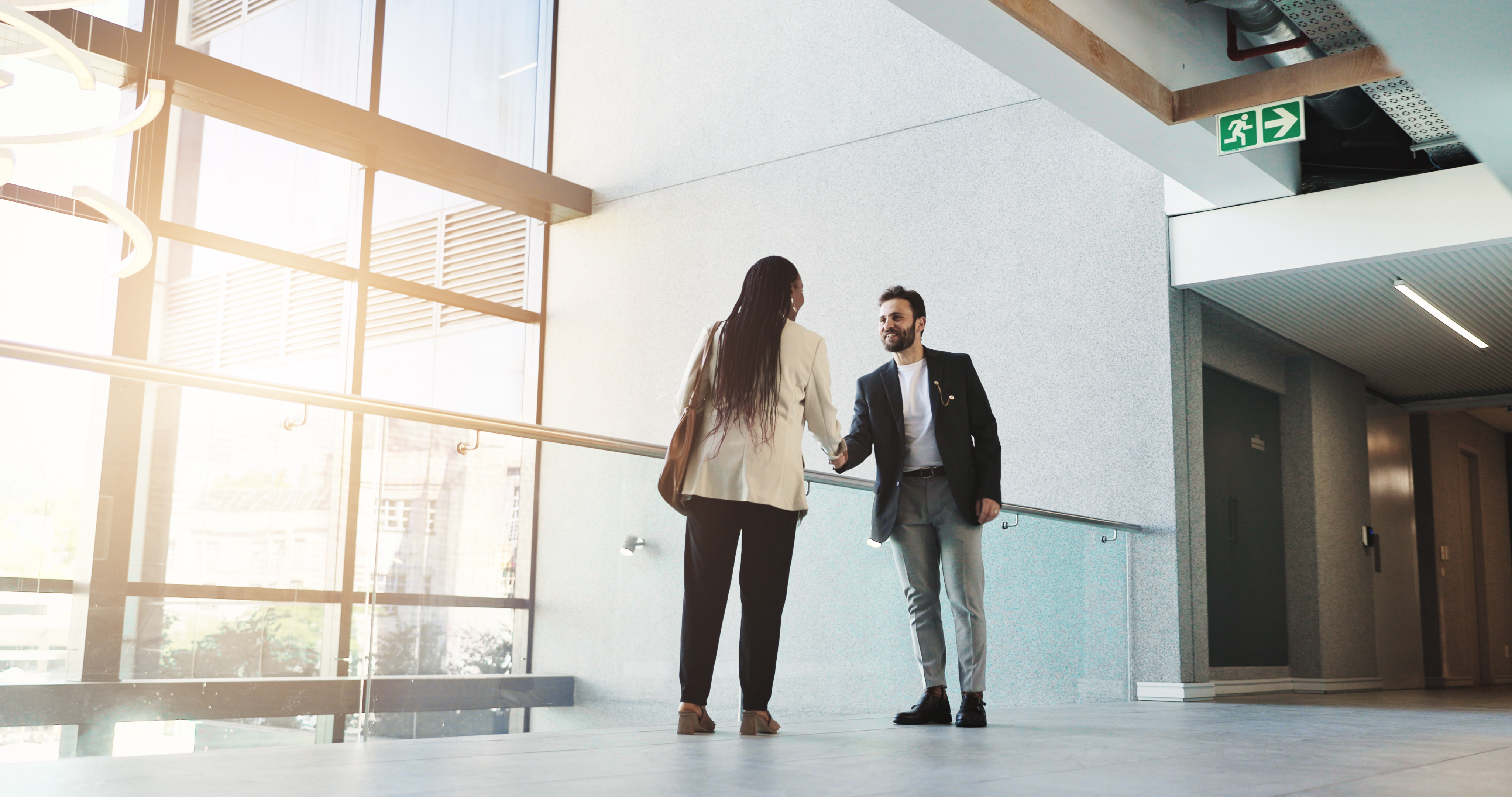 Two professionals greet each other with a handshake in a modern office building, symbolizing a successful interview or business meeting.