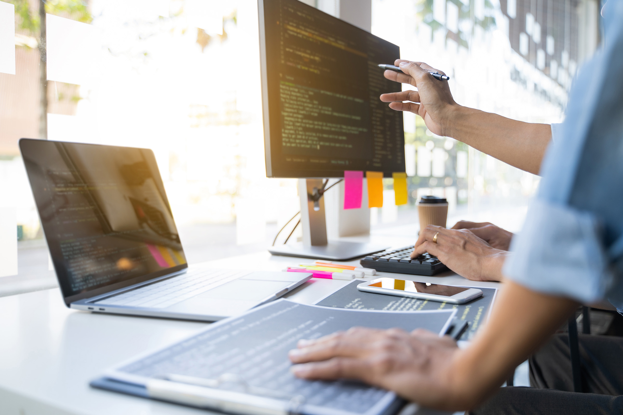 Two professionals collaborating at a desk with computer screens displaying code, notebooks, and digital tools—representing software development or data engineering work.