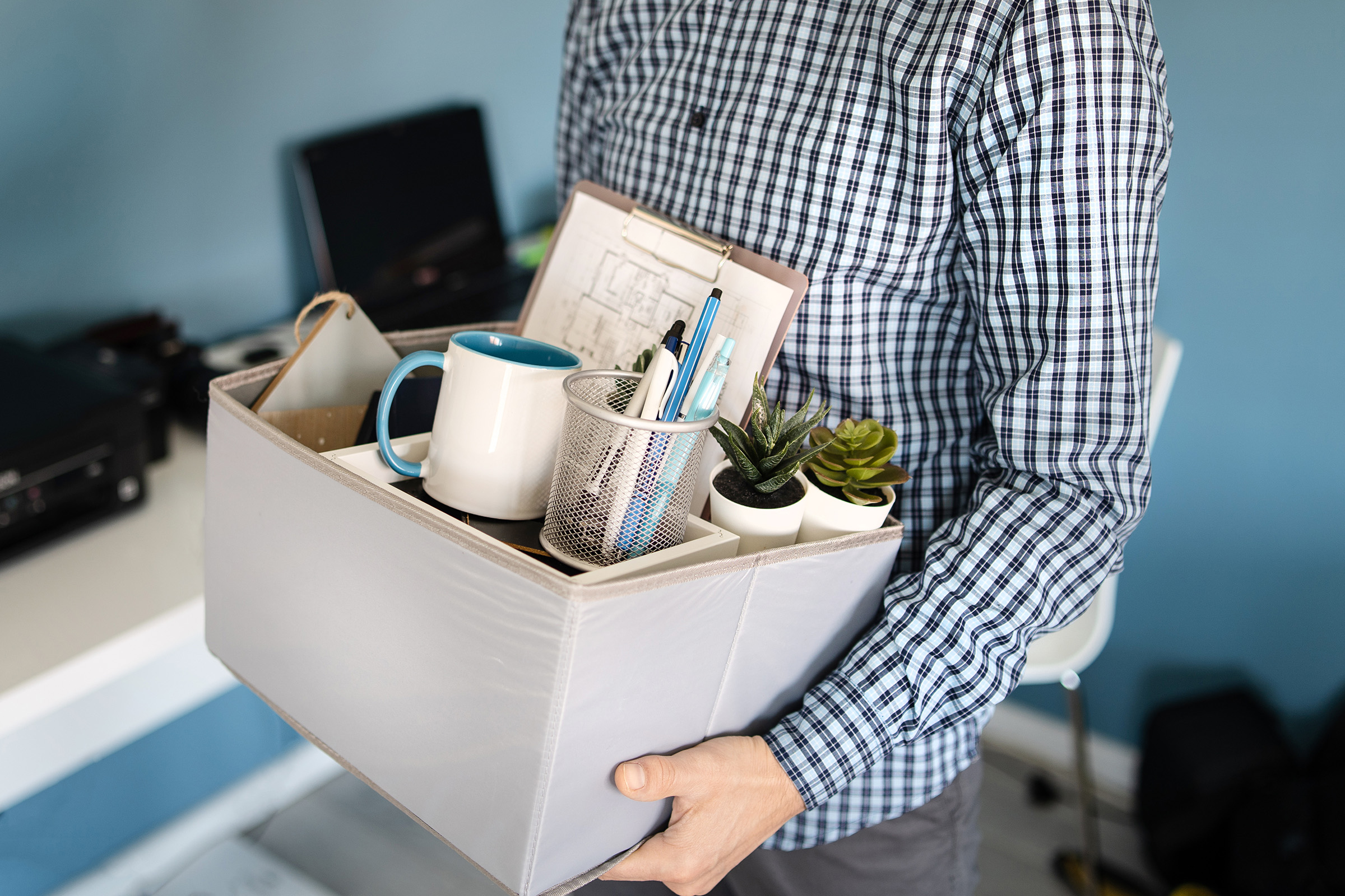 Employee holding a box of personal office items, including a mug and desk supplies, after leaving a job.