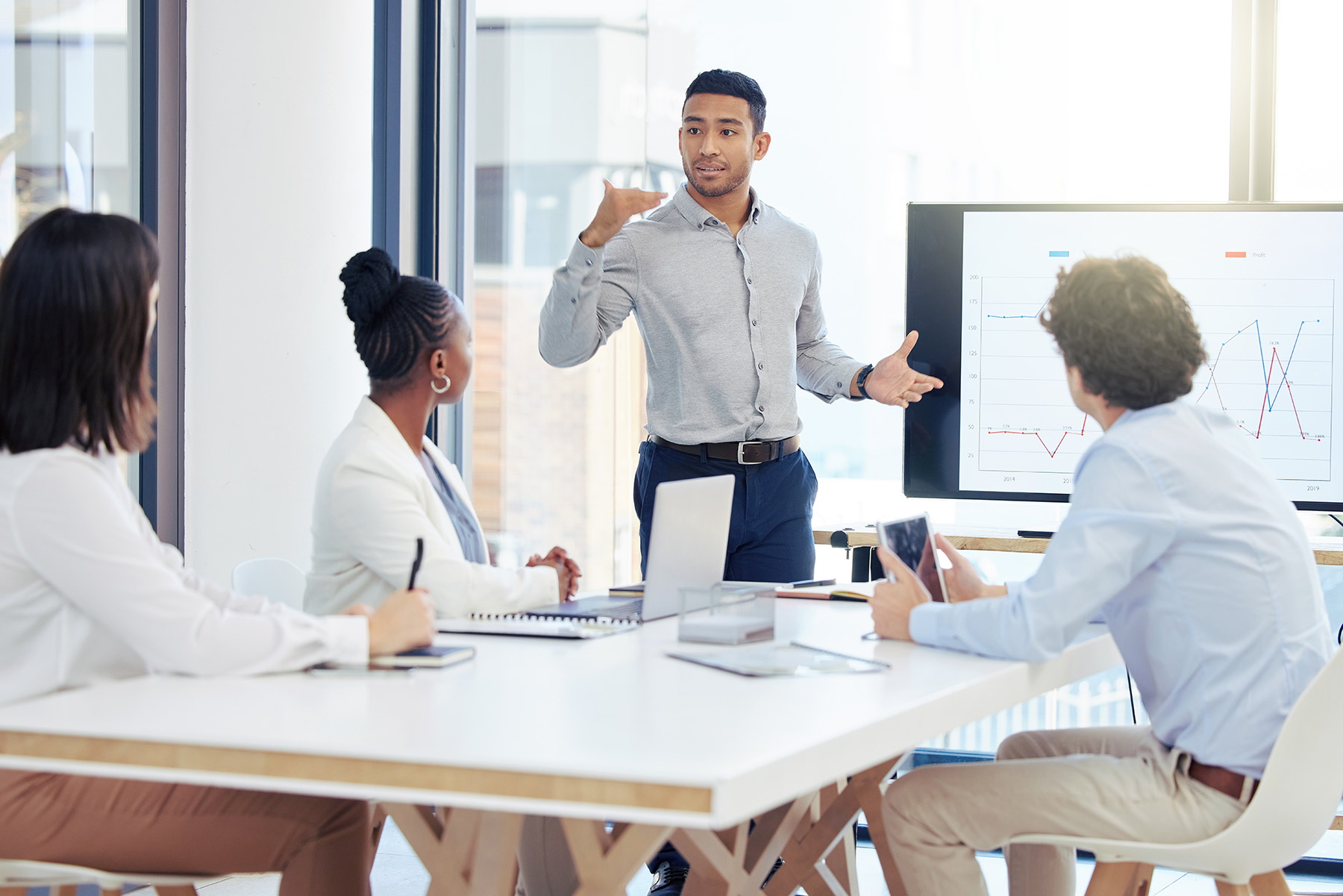 Business professional presenting data on a screen to a team during a collaborative meeting in a modern office