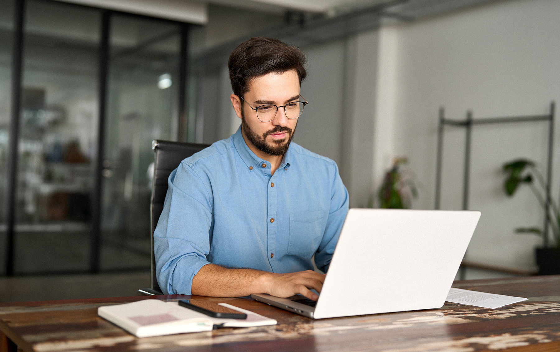 Professional man working on a laptop at a desk in a modern office workspace.