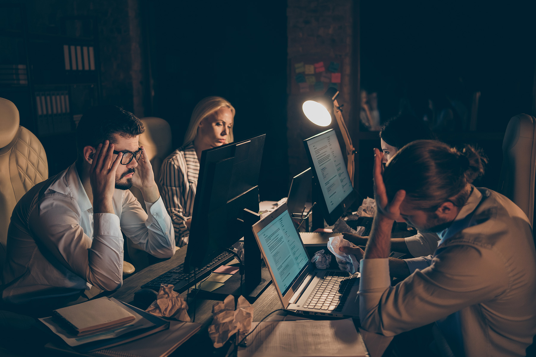 Overworked employees working late at night in a stressful office environment with computers and paperwork.