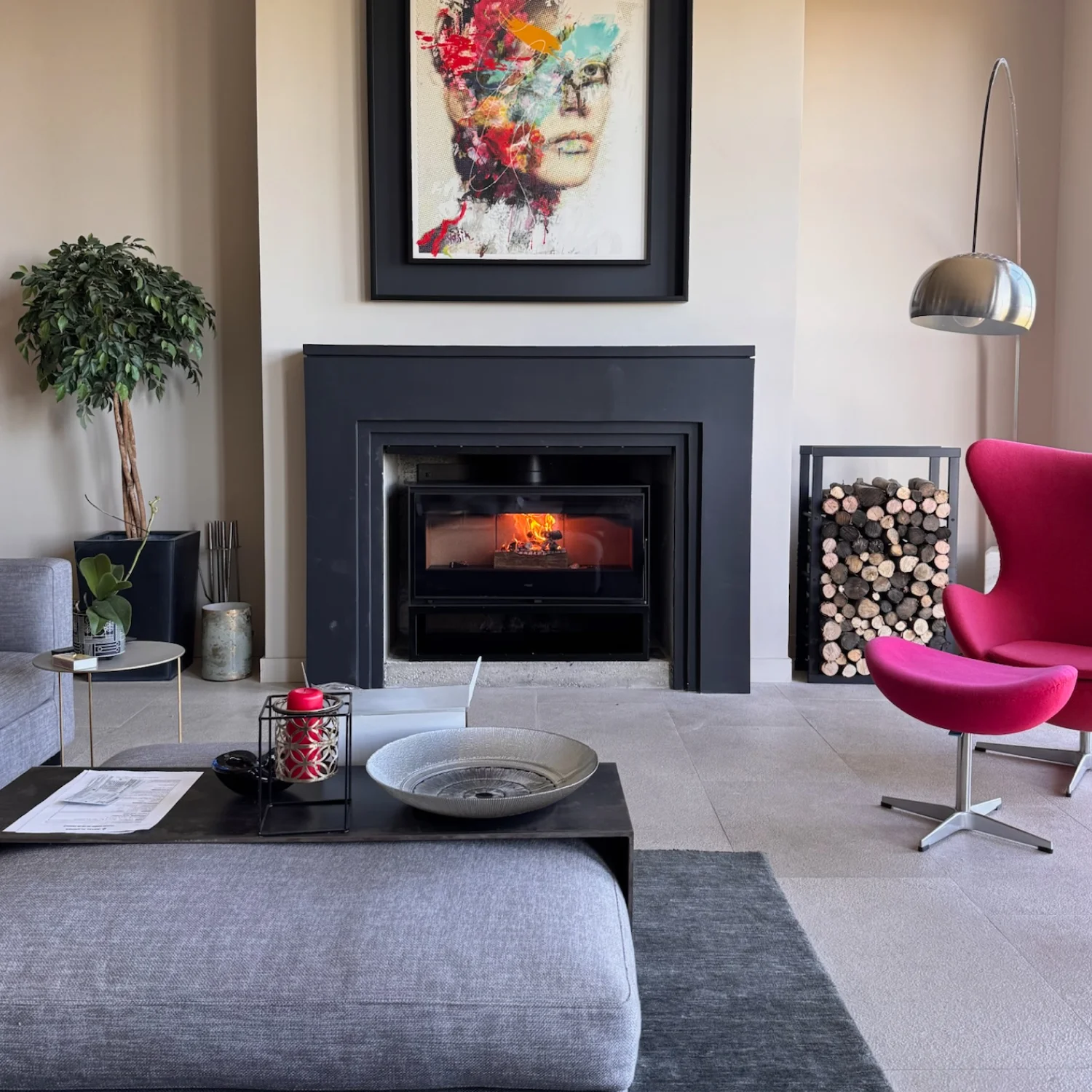 Salon moderne avec insert encastrable noir, fauteuil rouge, rangement à bûches et tableau coloré au mur.