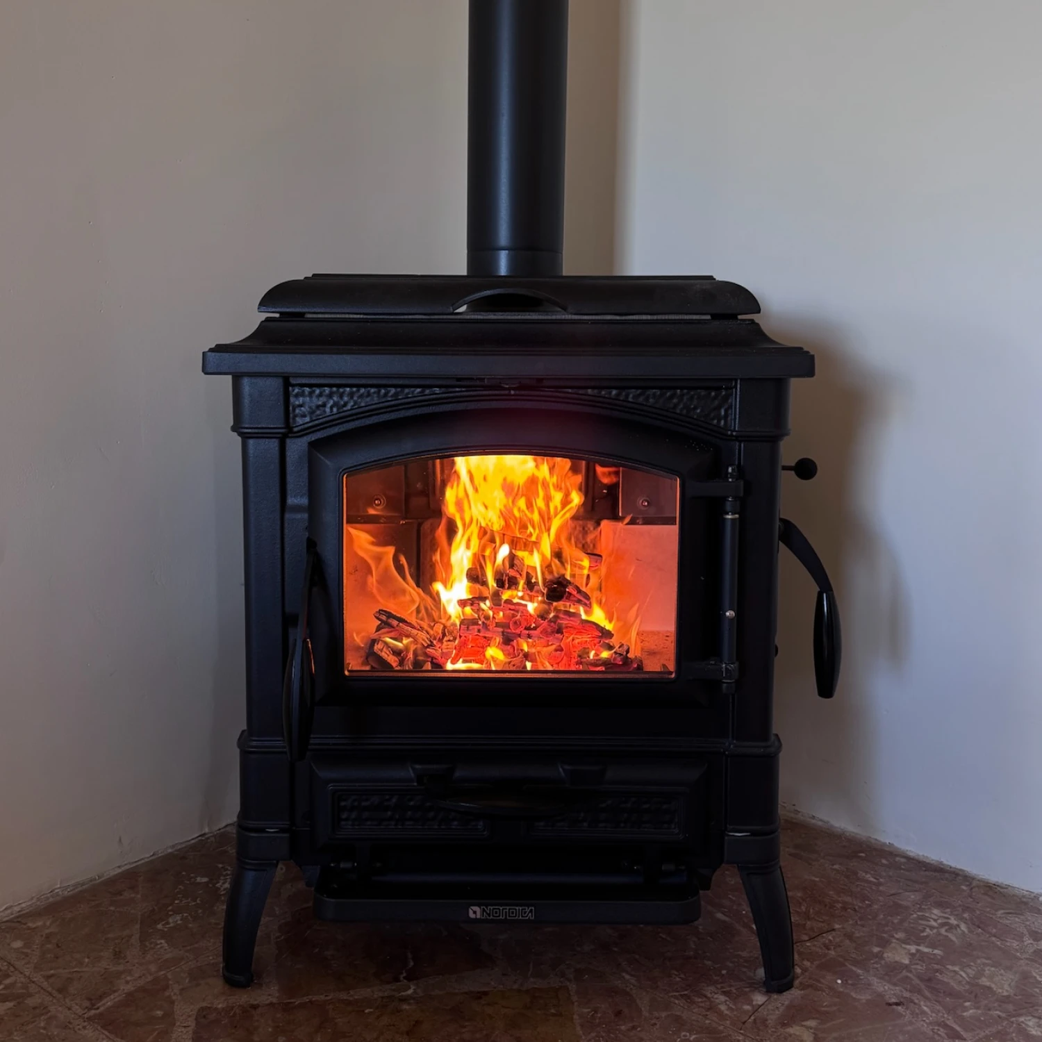 Poêle à bois noir avec feu brillant visible à travers une vitre encastrée dans un angle.