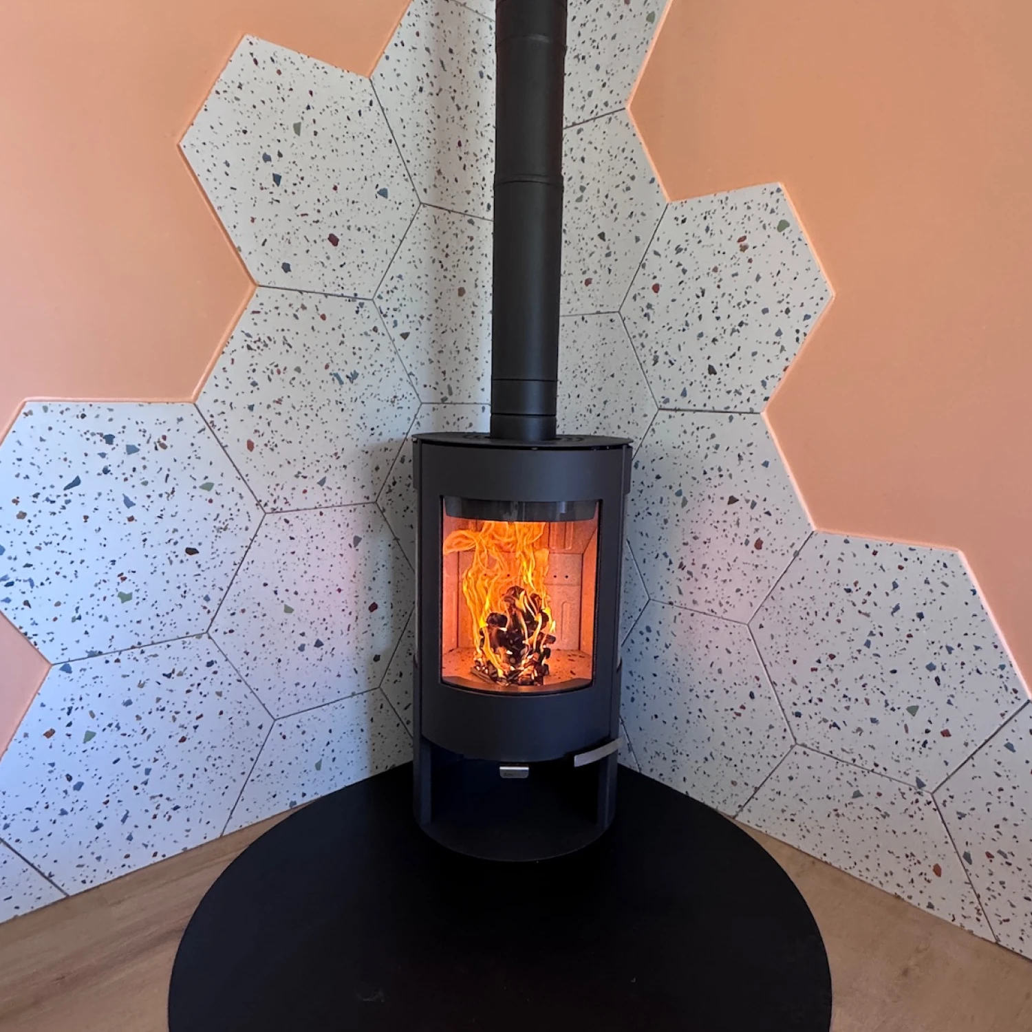 Poêle à bois moderne noir avec un feu vif, entouré de carreaux hexagonaux décoratifs.