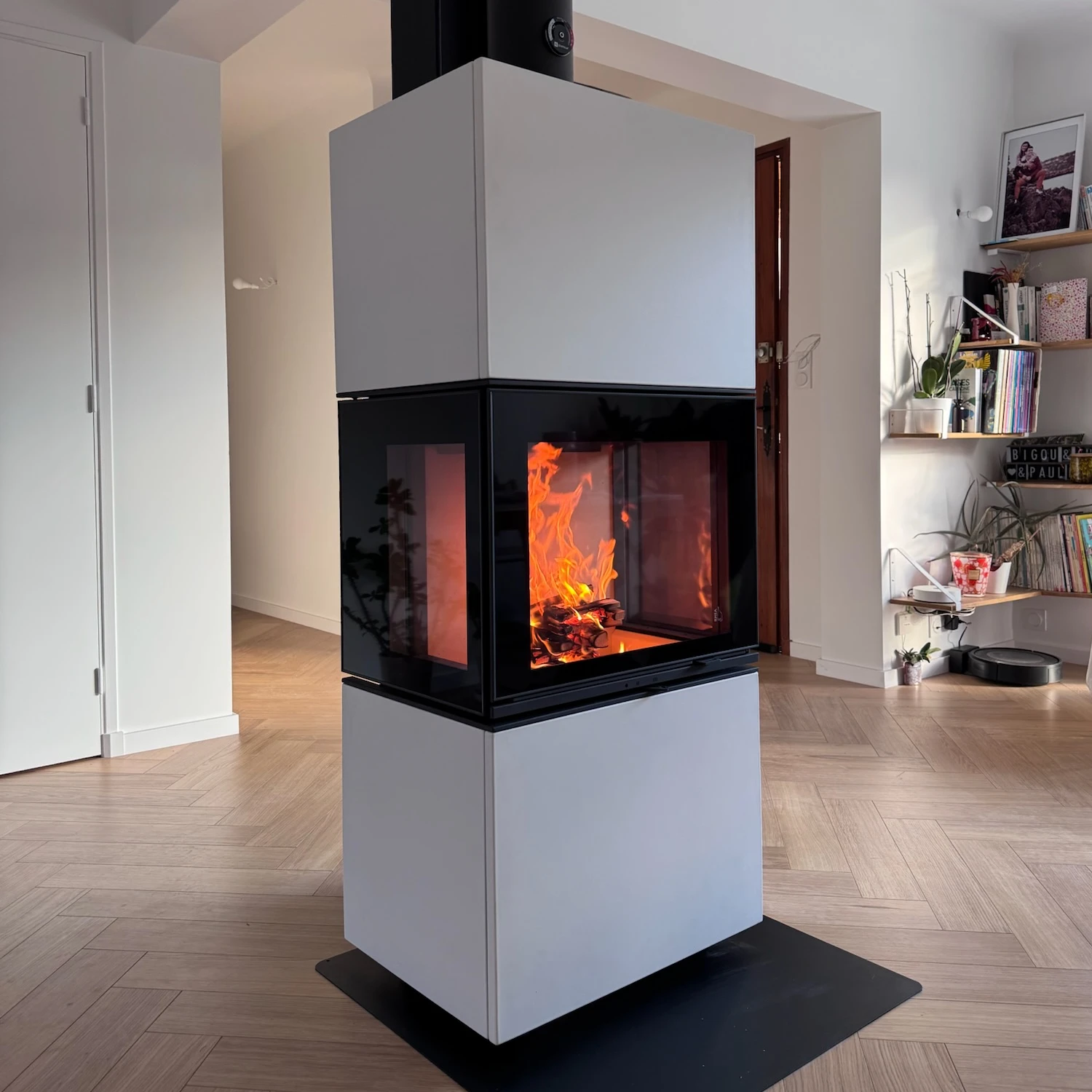 Poêle à bois moderne avec feu visible sur trois côtés dans un salon lumineux au sol bois.