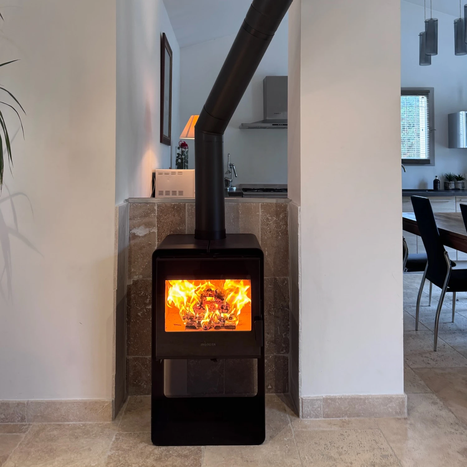 Poêle à bois noir allumé avec des flammes visibles dans un intérieur moderne clair.