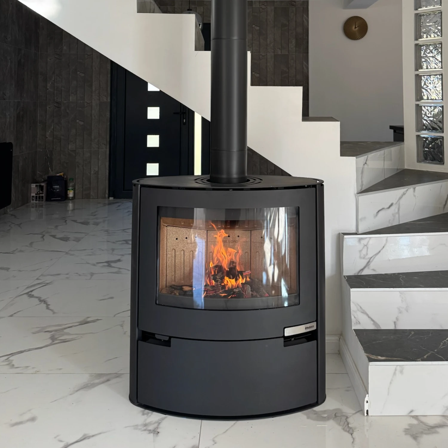 Poêle à bois noir moderne avec feu visible dans un intérieur élégant au sol en marbre blanc.
