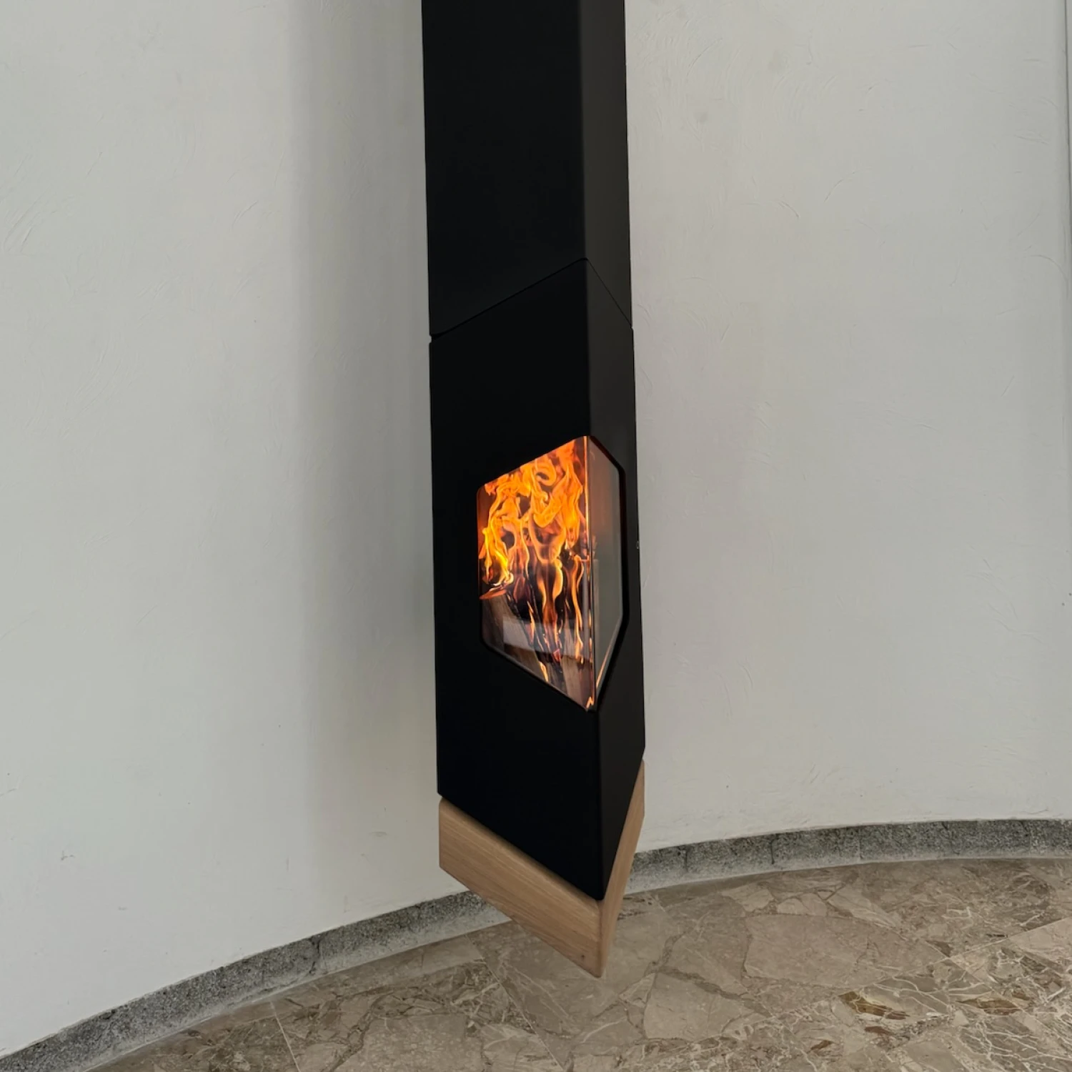Poêle à bois noir suspendu avec feu visible derrière une vitre et base en bois clair sur sol en marbre.
