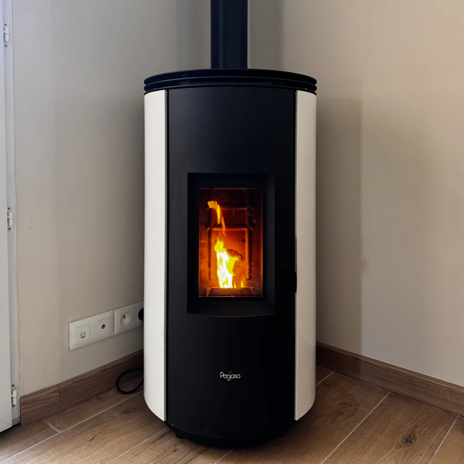 Poêle à granulés noir et blanc avec feu visible à travers une vitre, installé dans un coin de la pièce.