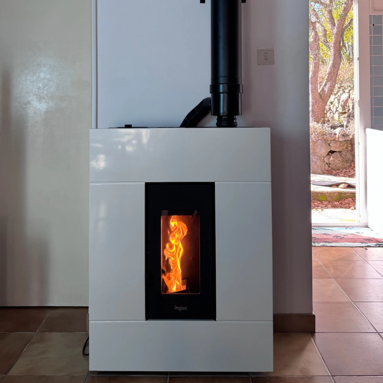 Poêle moderne à granulés blanc avec une flamme visible à travers la porte vitrée.