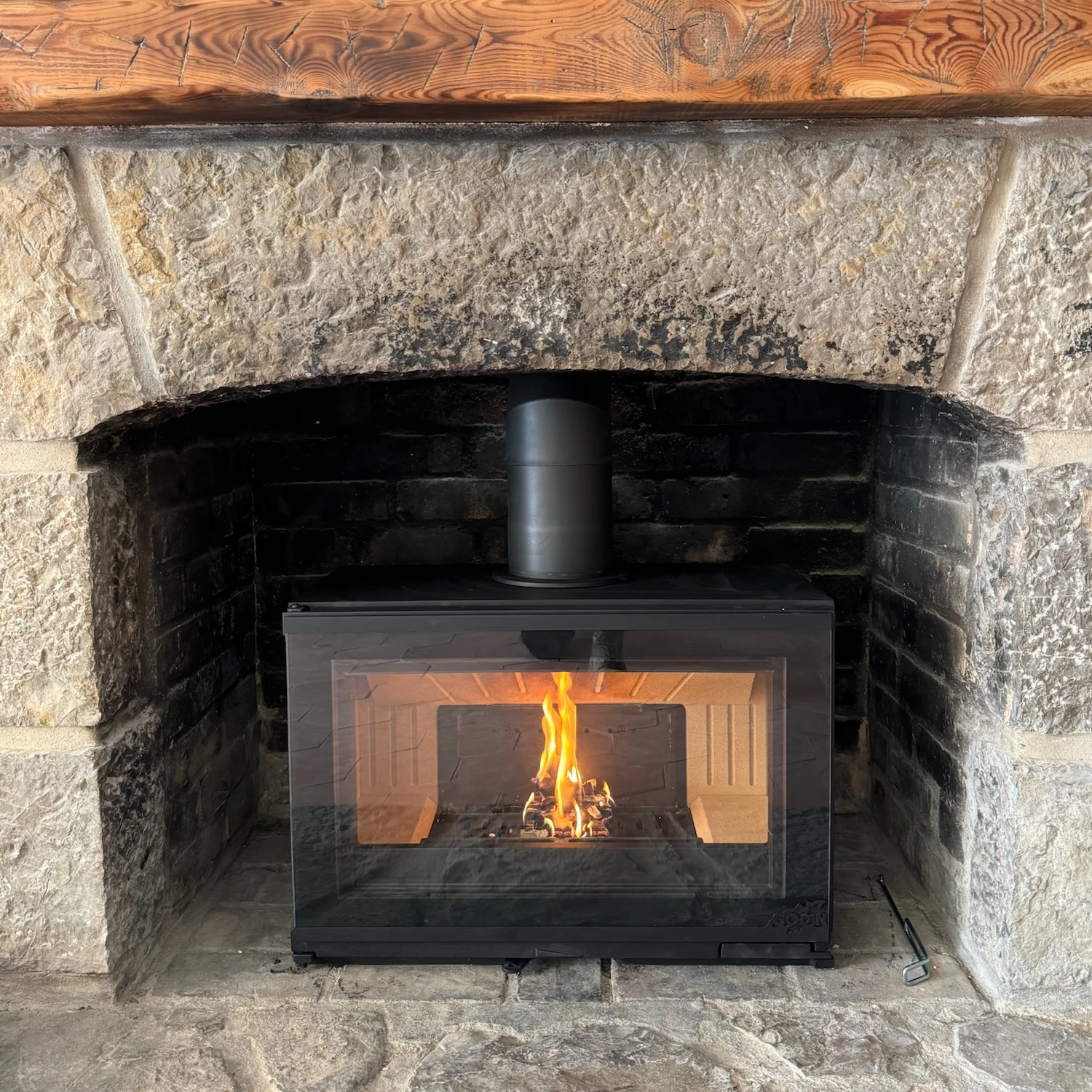 Insert de cheminée noir avec feu allumé dans une cheminée en pierre avec un cadre en bois.