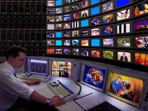 Man at a keyboard in front of a wall of TV monitors