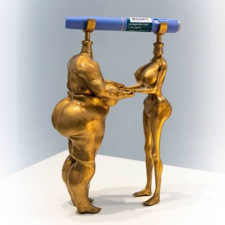 Gold sculpture of two figures holding up an injection pen