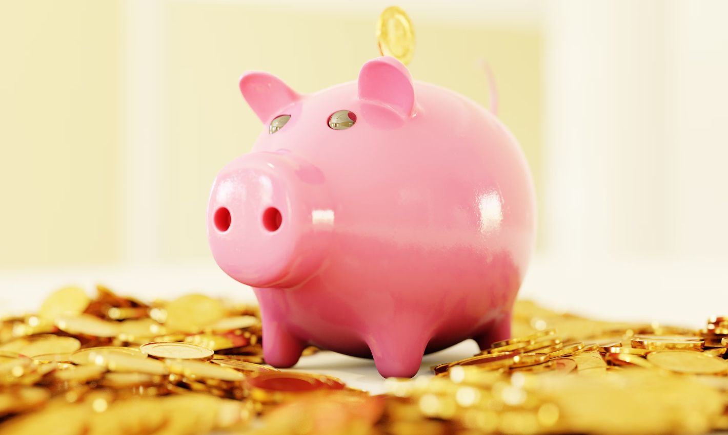 Pink piggy bank sitting on a pile of coins.