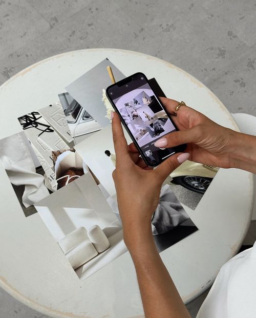 hands holding iPhone to photograph fashion images laying on a table