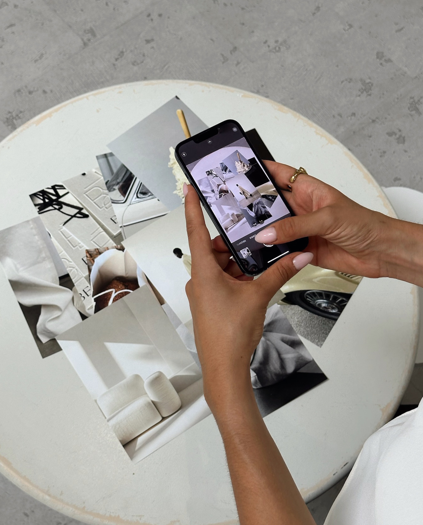 hands holding iPhone to photograph fashion images laying on a table