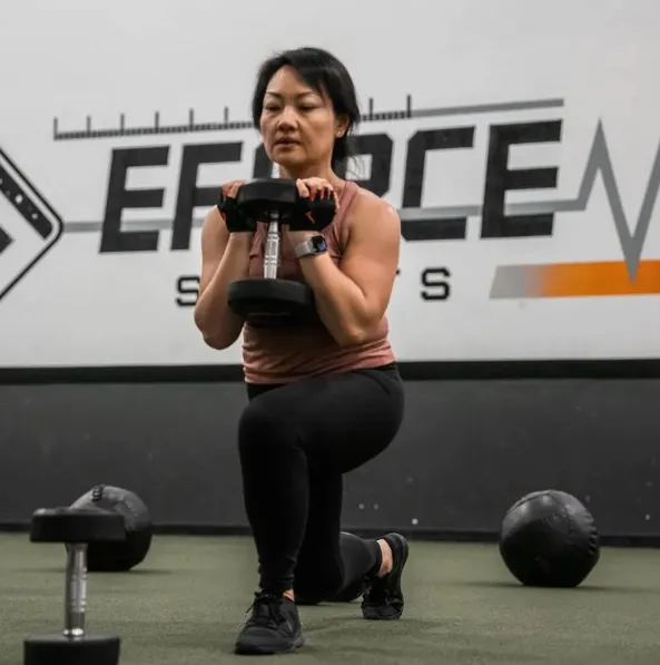 A woman squats with a kettle in front of her.