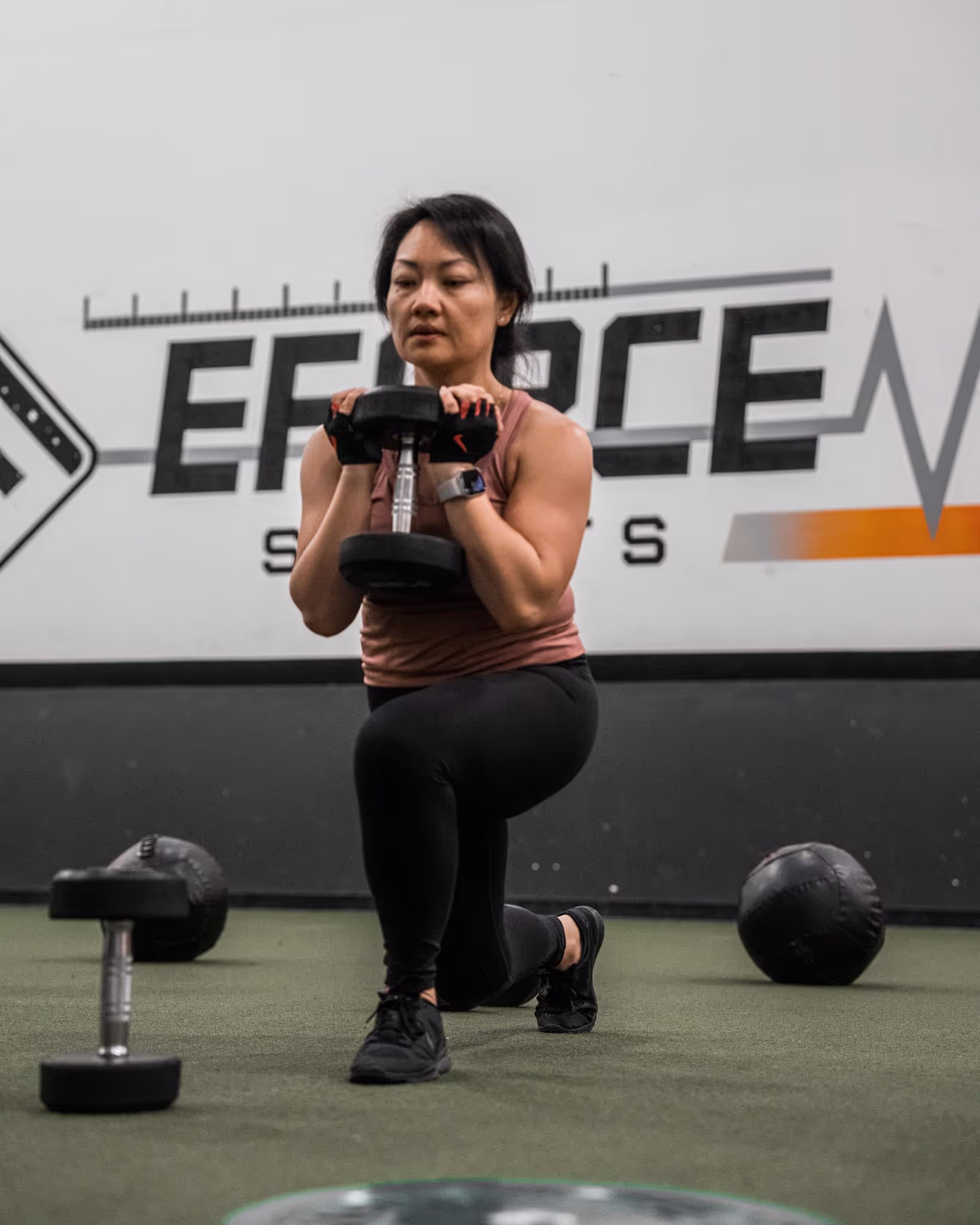 A woman squats with a kettle in front of her.
