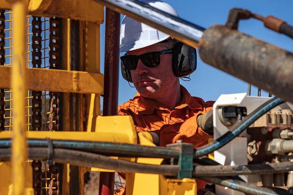 Construction or drilling technician wearing protective equipment operating industrial machinery and inspecting drilling equipment on-site.