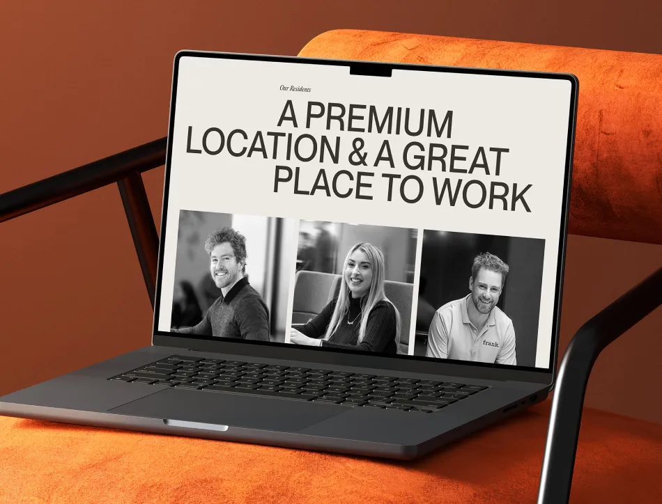 Laptop with keyboard attachment on orange background showing webpage with text "A PREMIUM LOCATION & A GREAT PLACE TO WORK" and black and white photos of business people
