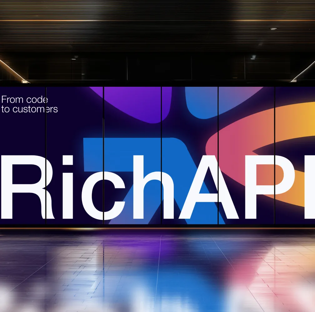 Large illuminated display wall showing "RichAPI" branding with text "From code to customers" and colorful gradient abstract shapes in purple, blue, pink, and orange on dark background in modern interior space