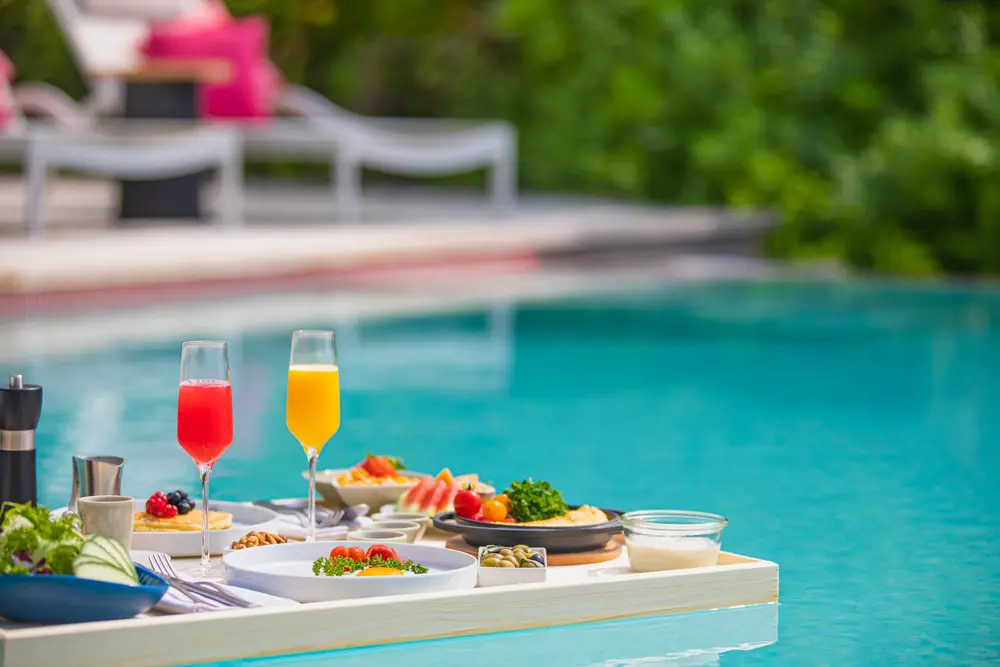 Luxury breakfast served on a floating tray in a pool at La Quinta by Wyndham, featuring colorful beverages and a variety of fresh foods.