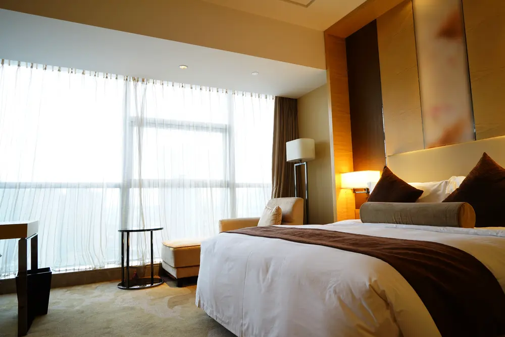 Elegant bedroom at The Residences at Biltmore - Asheville, featuring plush bedding, modern decor, and large window with sheer curtains.
