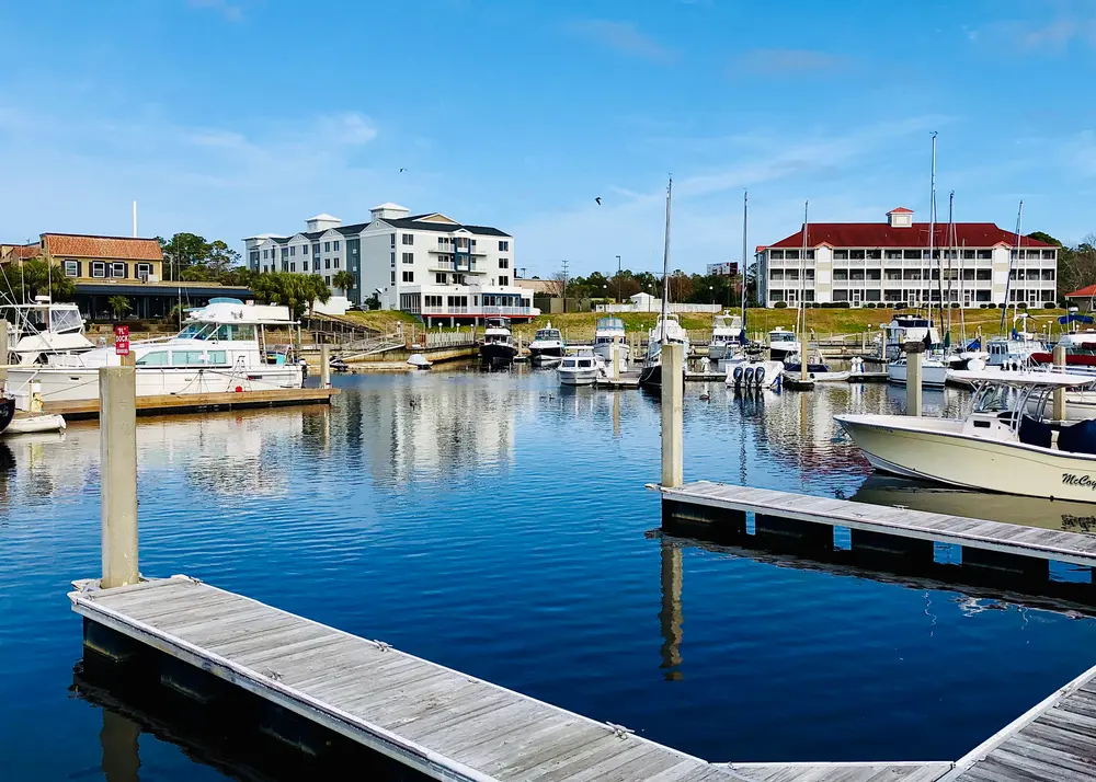Sunny marina view at Myrtle Beach with boats docked along piers and waterfront townhouses in the background.