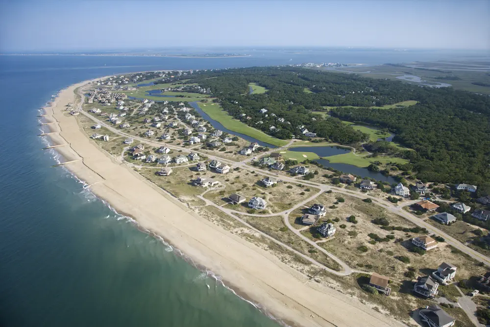 Aerial view of Bald Head Island shoreline with houses, sandy beaches, and greenery.