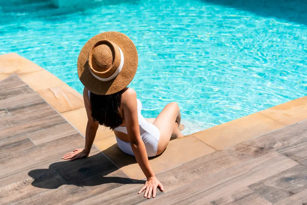 Woman lounging by poolside at Shutters on the Banks, in white swimwear and sun hat.