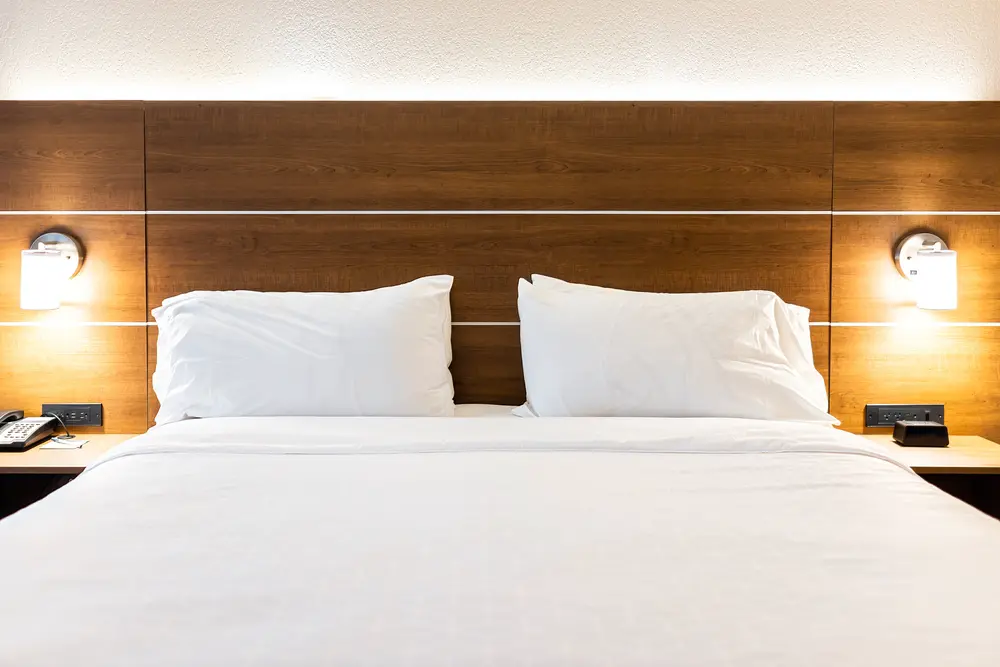 Alt text: "Elegant guest room at TownePlace Suites featuring a king-size bed with crisp white linens, flanked by wooden headboard and wall-mounted reading lights."