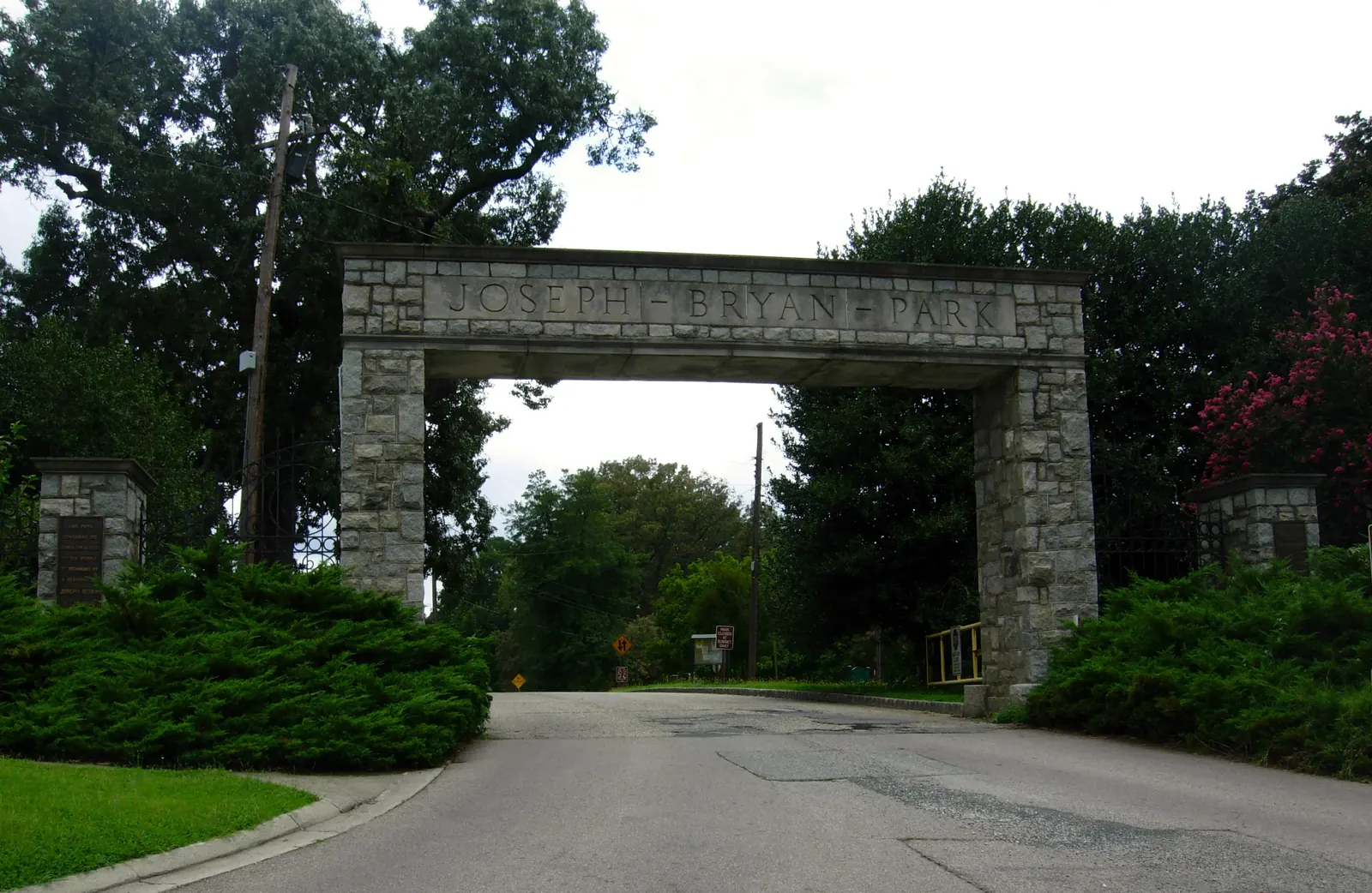 Stone gateway to Joseph Bryan Park with engraved name, surrounded by lush greenery and a roadway leading inside.