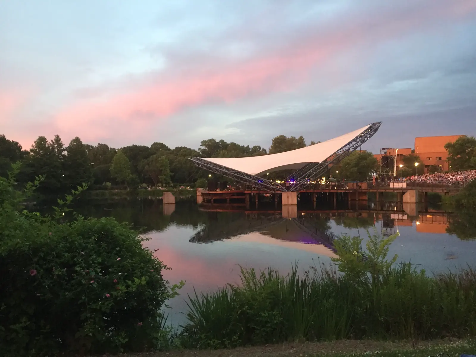 Twilight view of Charlotte Symphony Orchestra's outdoor amphitheater with a vibrant pink sky reflected in the water.