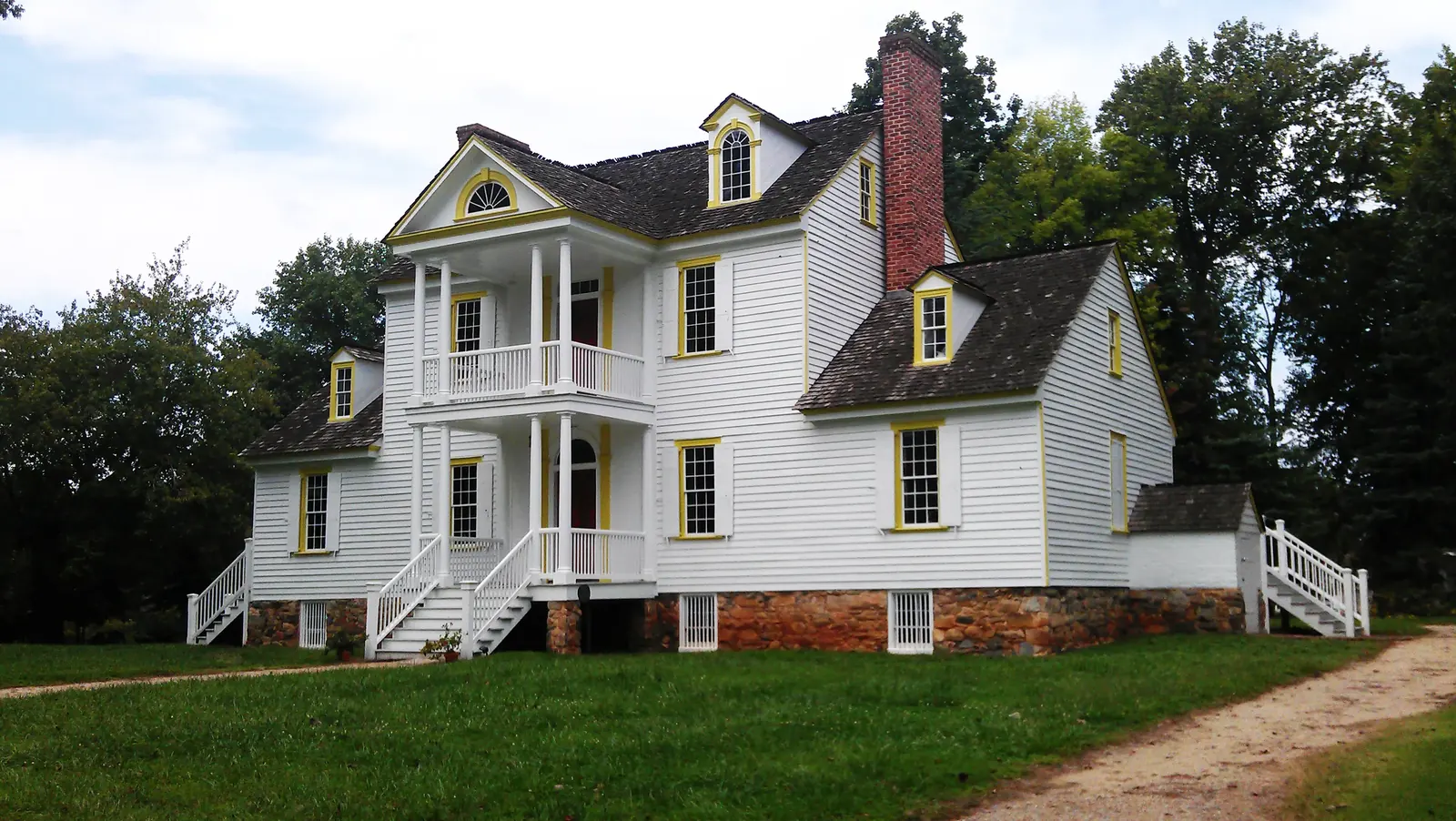 Two-story white colonial house with yellow trim, dormer windows, and surrounding greenery at Historic Rosedale Plantation.
